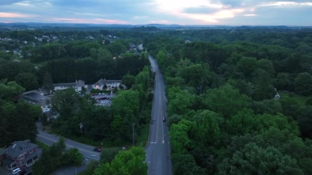 夕阳西下 一条笔直的长路上的空中拍摄 街道两旁有房屋 建筑物和树木 除了一辆汽车驶离外交通极少 — 图库视频影像