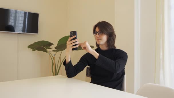 Young Man Glasses Waves Camera His Cell Phone Sitting Table — Stockvideo