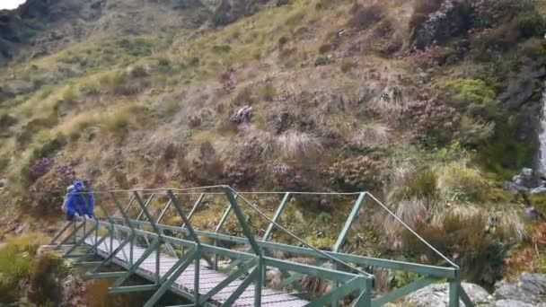 Pan Female Hiker Crosses Bridge Front Alpine Waterfall Routeburn Track — Αρχείο Βίντεο