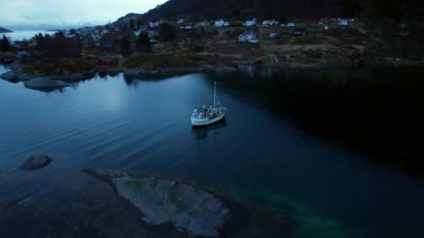 ノルウェー北部のフィヨルドの中にあるノルウェーの村を劇的な空で明らかにする漁船の軌道ビュー — ストック動画