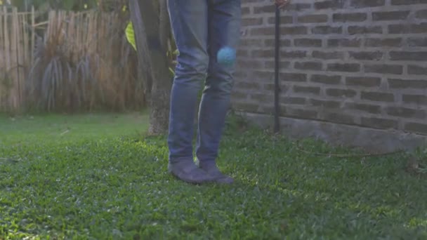 青いジーンズの男が家の庭に小さな青いボールを芝生の上で遊んでいる — ストック動画