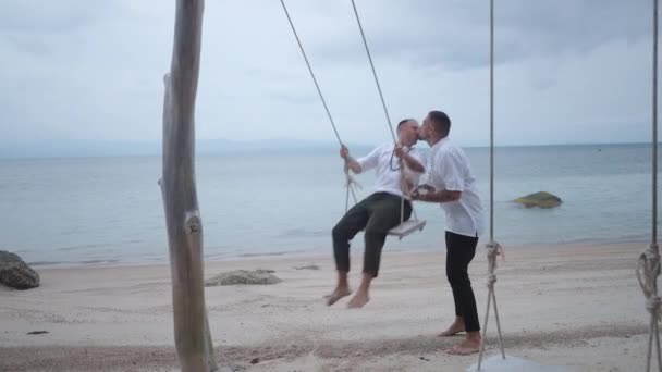 Lovely Male Gay Couple Honeymooners Kissing While Riding Beach Swing — Stockvideo