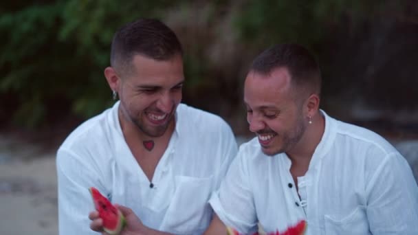 Diverse Gay Male Couple Eating Watermelon Together Talking Sitting Rocky — Stockvideo