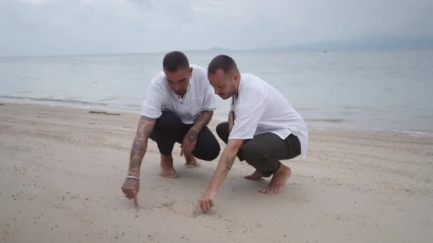 Займаючись Гей Пара Медоносців Малюють Форму Серця Піску Цілуються Пляжі — стокове відео