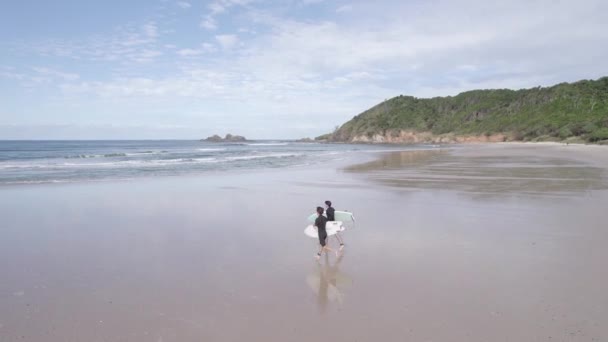 サーフボードを持つ2人の若い男性サーファーがオーストラリアのニューサウスウェールズ州の壊れた頭をサーフするために海にビーチで走っています 空中Fpv — ストック動画