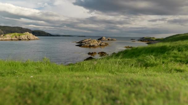 風が風と暗闇の中で草の吹きの緑のブレードとして海の表面に波を吹いている場合は 低カメラの角度は 気分の雲が日没時にオーバーヘッドを渡します スコットランドの半田島 — ストック動画