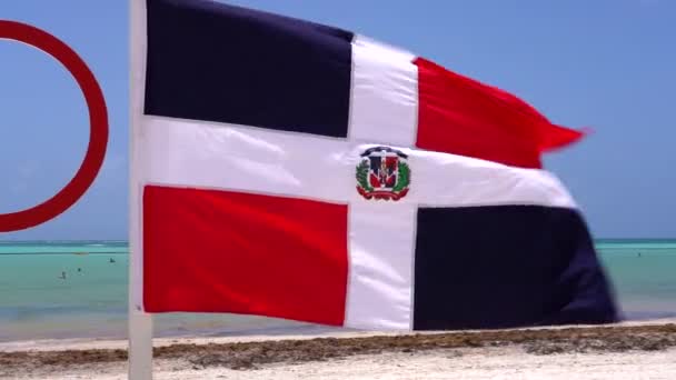 Dominican Republic Flag Waves Wind Caribbean Beach Tourists Walk White — стоковое видео