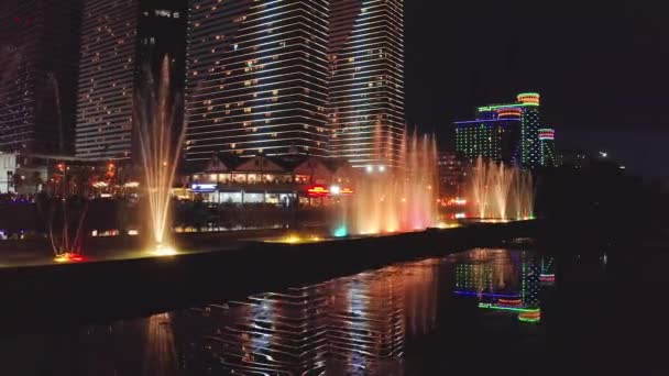 Brightly Lit Dancing Fountain Illuminated Skyscrapers Reflected Lake Night — стоковое видео