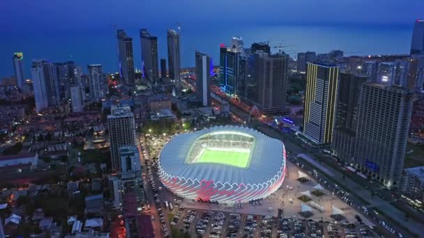 Близкий Подход Беспилотника Освещенному Спортивному Стадиону Среди Города Ночью — стоковое видео