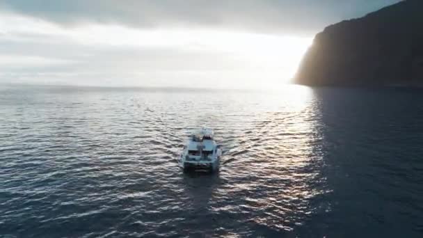 カタマランヨットは ポルトガルのマデイラ島で日没時にフンシャル湾近くの平和な海を航海します 空中プルバックショット — ストック動画