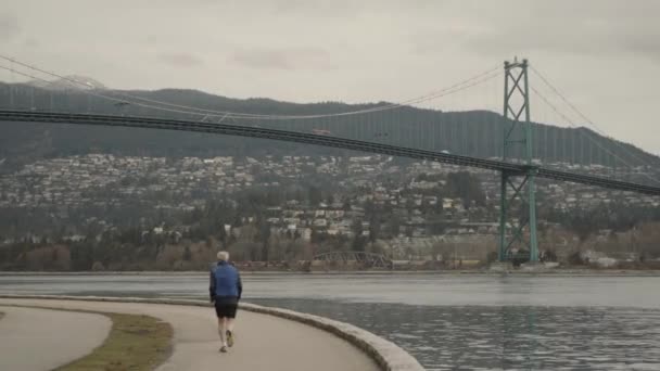 Wide Panning Shot Running Man Stanley Park Lions Gate Bridge — стоковое видео