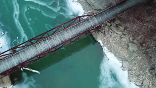 Rusty Footbridge Icy Mountain River Top Drop Drone Shot — Stockvideo