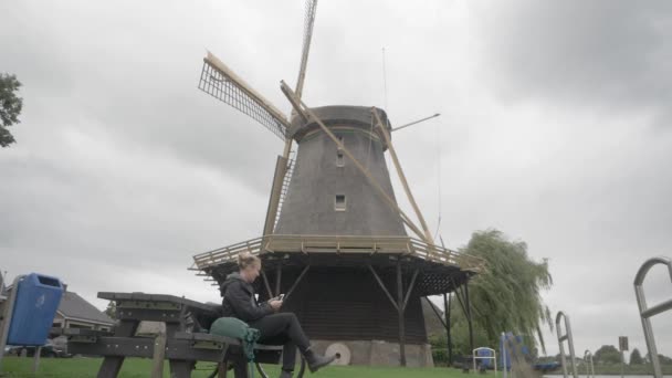 荷兰的旅游业 一位年轻妇女坐下来拍摄了一张老风车的照片 — 图库视频影像