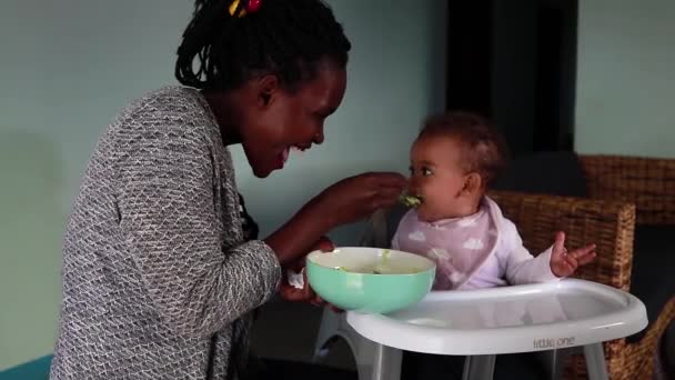 アフリカ人女性フィード彼女の赤ちゃんの娘ながらで高い椅子 — ストック動画