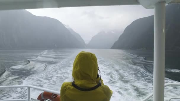 ニュージーランドのボートからミルフォードサウンドのフィヨルドを撮影した鮮やかな黄色のレインジャケットの女の子 — ストック動画