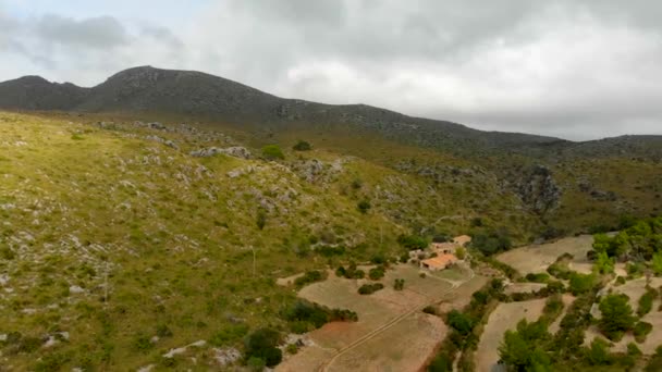 緑の丘といくつかの建物が前景にある山に向かって移動するドローン映像 4Kでリアルタイムで撮影 — ストック動画