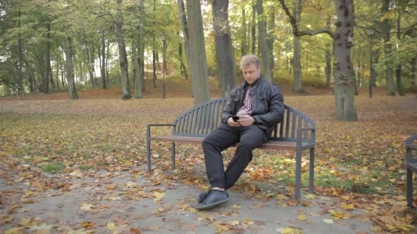 Young Attractive Male Sitting Park Bench Using His Smart Phone — Stock Video