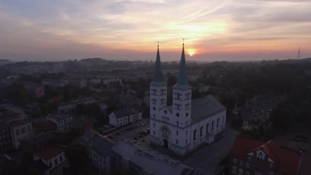 霧深い日の出の間に小さなヨーロッパの町でキリスト教の教会の空中旋回ショット — ストック動画