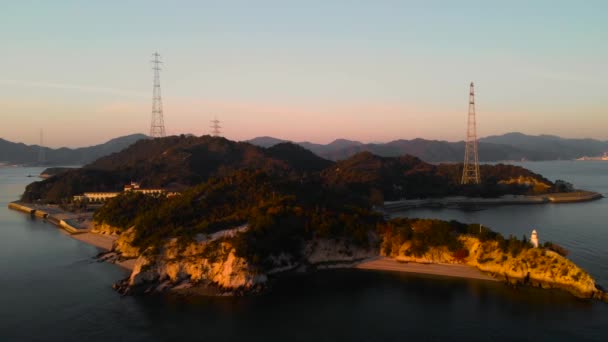 Backwards Aerial Drone Movement Island Lighthouse Powerlines Sunset — Stock videók