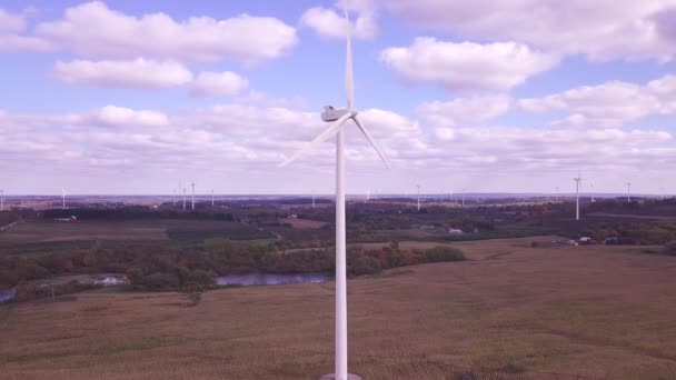 風力タービンの空中ビューは 緑と再生可能エネルギーを作成します 畑や池を背景にエネルギーを生み出すタービンの回転とともにカメラビューは左右に回転しています — ストック動画