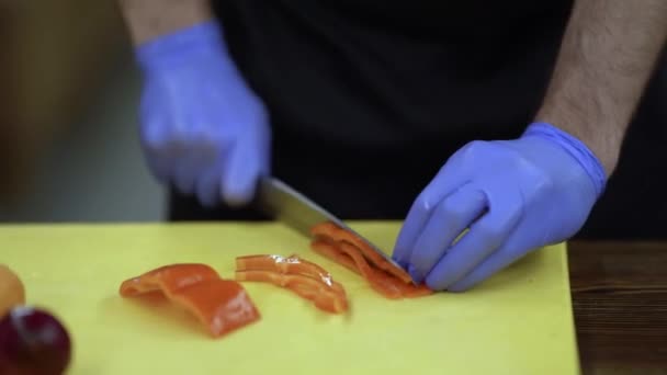 烹饪过程中的近距离镜头 戴着手套的炊具把红辣椒精细地切碎在木板上 然后放进一个煎锅里 又是一片蔬菜 — 图库视频影像
