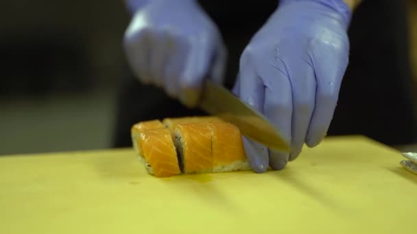 フィラデルフィアの寿司ロールのクローズアップビデオ 料理人はそれをカットし 小さな等しい部分を作ります その後 寿司ロールを引き締めるためにチーフはローリングマットを使用しています 背景がぼけている — ストック動画