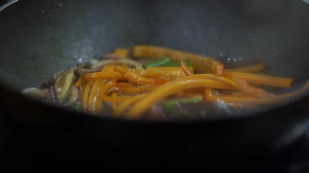 烹饪过程中的近距离镜头 切碎的蔬菜 胡萝卜 芦笋和洋葱 正在锅里煎 戴手套的厨师把他们和秃头混在一起 — 图库视频影像