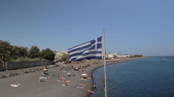 Amplo Tiro Praia Kamari Santorini Com Uma Bandeira Grega Batendo — Vídeo de Stock