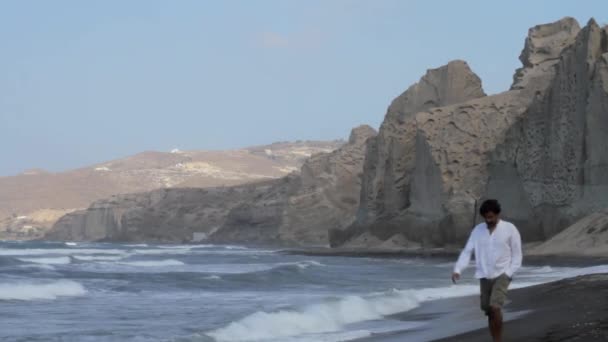 Homem Está Caminhando Sozinho Uma Praia Areia Preta Cercada Por — Vídeo de Stock