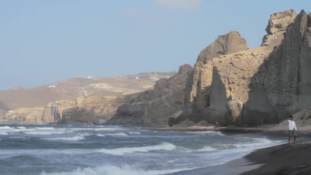 Uomo Solo Una Vasta Spiaggia Sabbia Nera Circondata Formazioni Scogliere — Video Stock