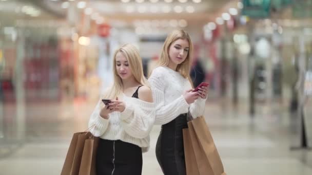 Two Pretty Blonde Girls Hold Smartphones Shopping Bags Stand Hall — Stockvideo