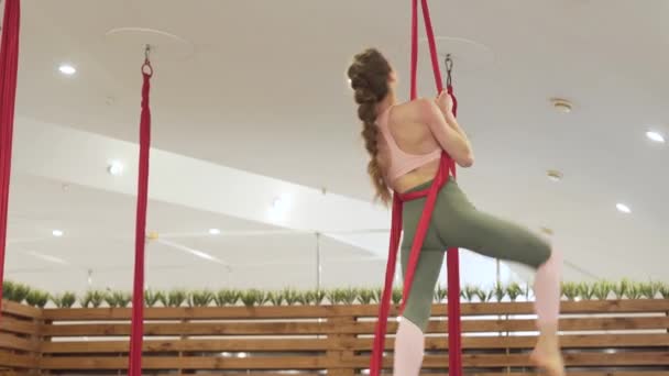 穿着紧身裤和粉色上衣的健康女孩练习飞舞瑜伽 女运动员抬起头来 在空气中做着完全分开的动作 把腿放在一起 做着背部弯曲的动作 脚上滚动着吊床 — 图库视频影像