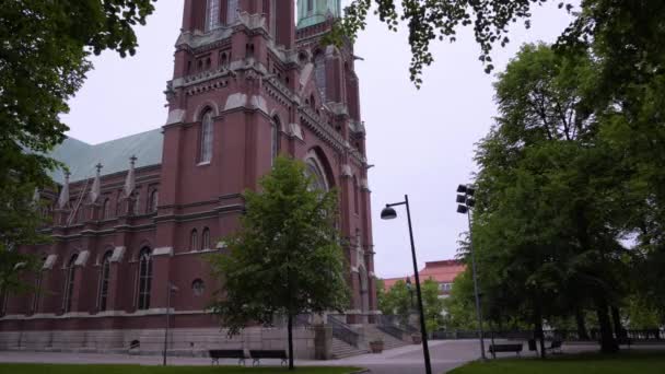在芬兰赫尔辛基乌兰林纳的一个阴沉沉的夏日里 圣约翰教堂的静态镜头 拍摄在绿树下 树枝下 长满了树叶 挂在窗框上 — 图库视频影像
