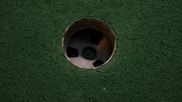 一只紫色迷你高尔夫球的近距离鸟瞰掉进了高尔夫球洞里 在球场上的口袋里弹跳着 — 图库视频影像