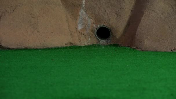 Orange Mini Golf Ball Exits Pipe Wall Rolls Misses Hole — Stock Video
