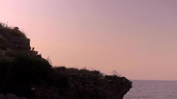 Two Silhouetted People Sitting Cliff Backlit Pink Sunset Sky Amalfi — Vídeos de Stock