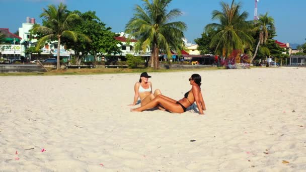 在泰国的一个阳光明媚的日子里 两个年轻女子一起沐浴在一个充满异国情调的海滩上 度假胜地附近长着白沙和棕榈树 — 图库视频影像