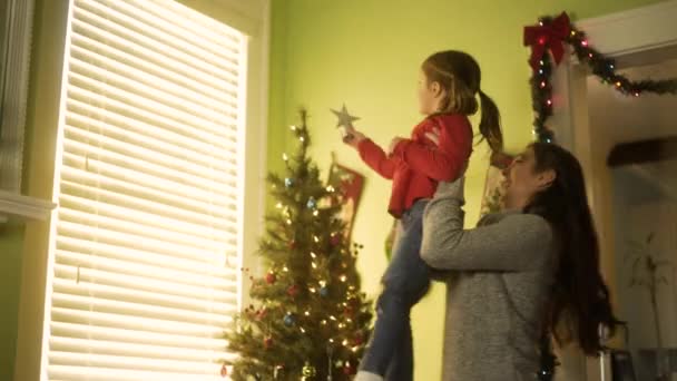 母亲把女儿举起来 把星星放在宽阔的圣诞树顶上 — 图库视频影像