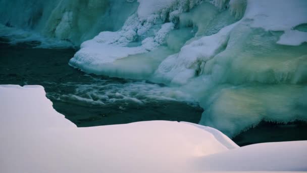 冬の氷結した風景の中を流れる小川の氷に覆われた銀行 遠くのフィヨルドに向かって平和的に流れる氷や氷河の泡の小川 冬の不思議の国の森の風景 — ストック動画
