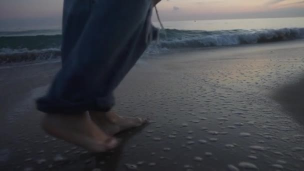 Dziewczyna Spacerująca Boso Długich Dżinsach Wzdłuż Brzegu Plaży Podczas Zachodu — Wideo stockowe