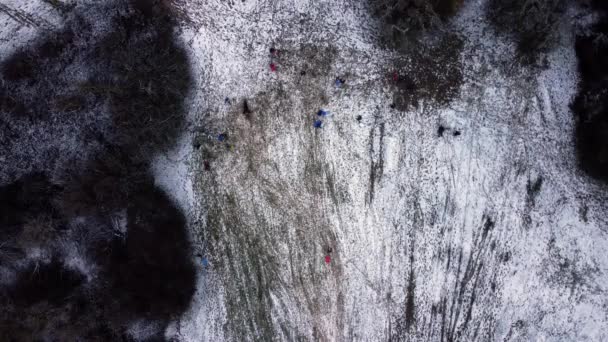 快乐的孩子和成年人 在雪地的斜坡上滑行 在一个宁静的冬日里玩得开心 从上往下的静态无人机 — 图库视频影像