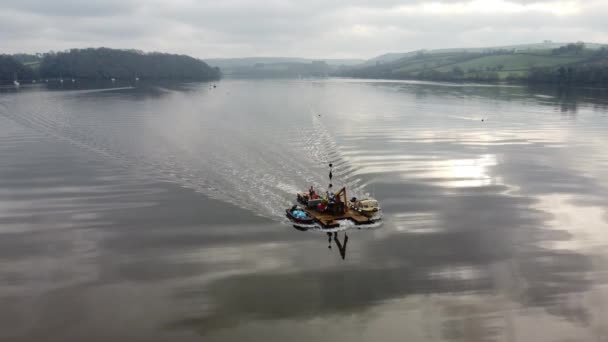 一艘小型工作船拖着一艘装有起重机的驳船驶过船架 船架后面是一条静止不动的河流和乡村 — 图库视频影像
