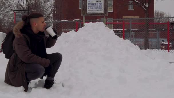 モントリオールのローズモント バラの雪の公園でひざまずいて若い男は暖かいコーヒーやホットチョコレートを飲みます 冬に外で熱い飲み物を飲む男 — ストック動画