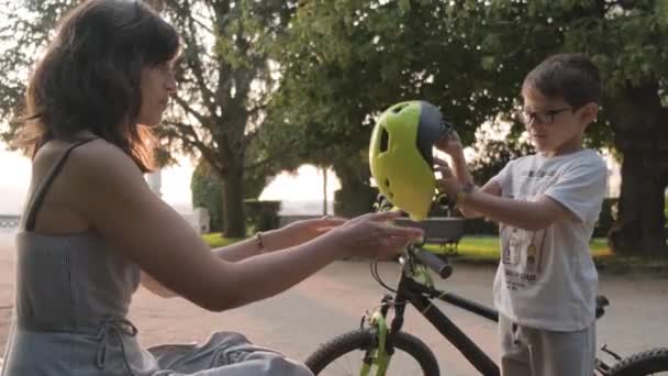 母親は息子に自転車に乗る前に着る自転車用ヘルメットを与えます — ストック動画