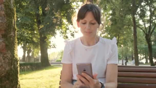 Μια Γυναίκα Που Χρησιμοποιεί Τηλέφωνό Της Ενώ Κάθεται Στο Πάρκο — Αρχείο Βίντεο
