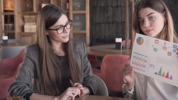Two Charming Young Woman Presentating Some Data Looking Directly Camera — Vídeo de Stock