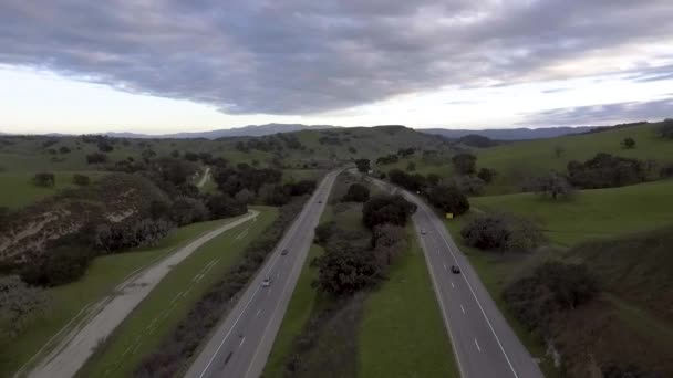 高速道路101号線の上を飛ぶドローンは緑豊かな丘の両側に車が行くのを見て忙しいパスを囲む — ストック動画
