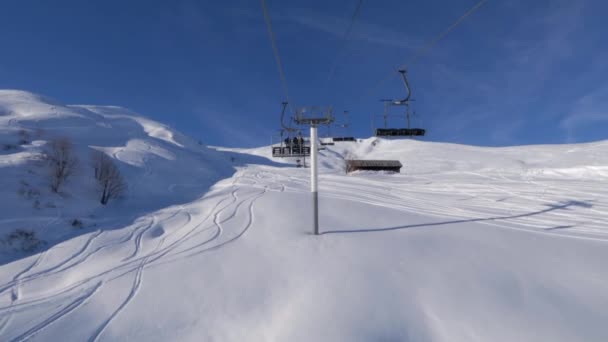 明るい青空と白い新雪を持つ山の中のスキーリゾートでチェアリフトに乗る — ストック動画
