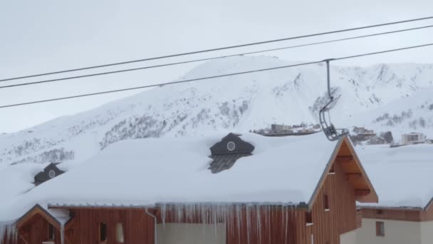 背景の屋根に雪と山の中でスキー場で実行されている空のリフト — ストック動画