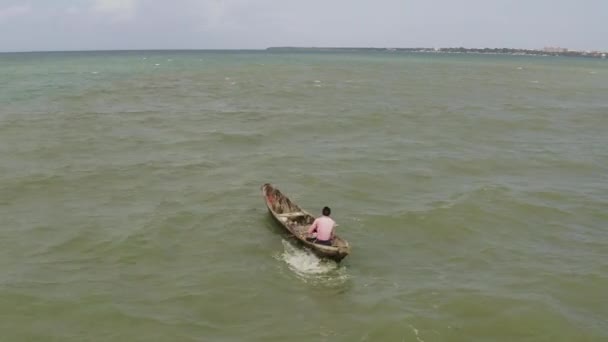タンザニアの晴れた日にダルエスサラームの海岸近くで波と風に対して木製のカヌーボートを漕ぐ男 — ストック動画